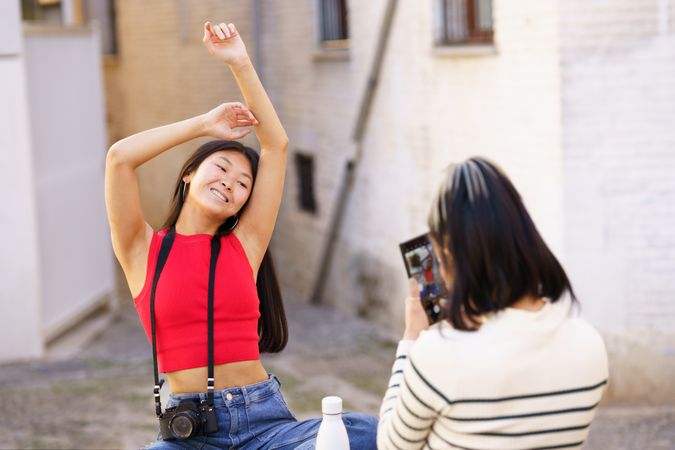 Woman smiling with arms above her head as her friend takes her picture