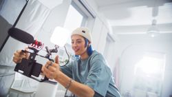 Young Female Filmmaker With Blue Hair, Wearing A Beanie, Operates A Professional Camera In A Well-lit Studio, Capturing Engaging Content For A Creative Advertising Project.