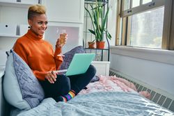 Happy Black woman smiling at a laptop with champagne flute in light filled living room