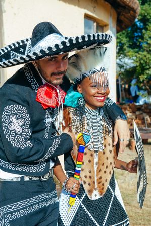 Groom in traditional Mexican outfit embracing bride in traditional Zulu attire
