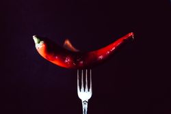 red chili pepper on fire in fork on a dark background