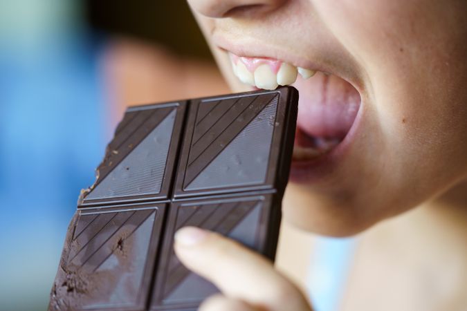 Girl biting into square of dark chocolate