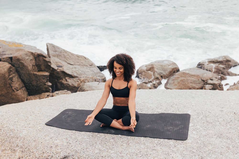 Happy woman sitting meditating next to the ocean