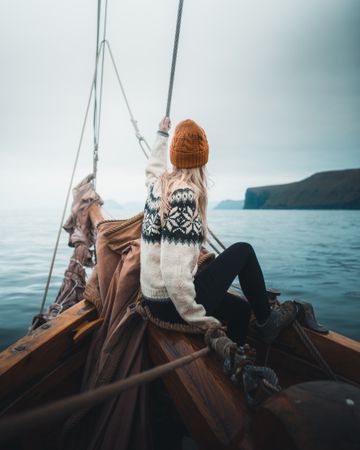Woman wearing sweater sitting on boat on sea