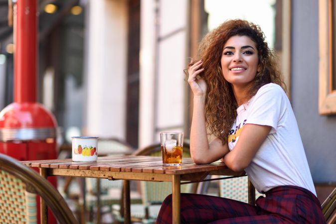 Carefree Arab woman in casual clothes drinking a soda on cafe patio