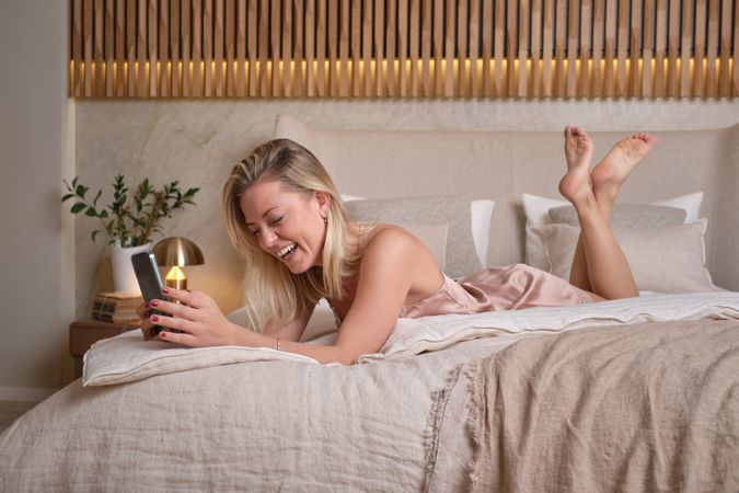 Laughing female browsing smartphone in bed