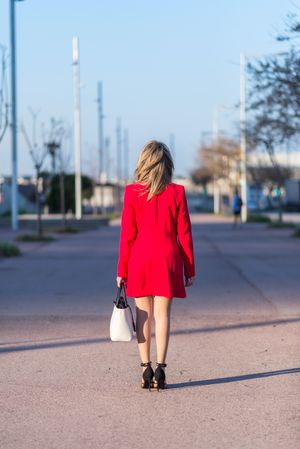Back of woman in red coat and heels standing on street
