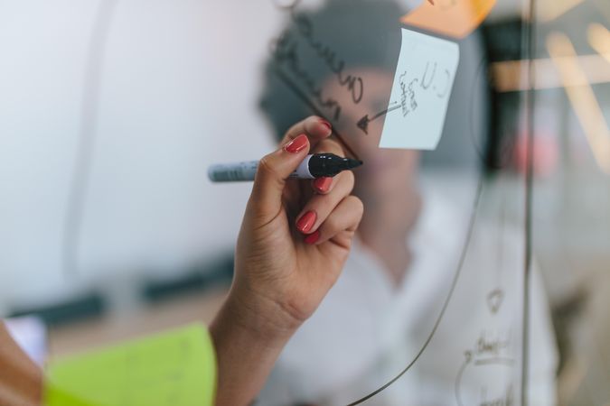Close up of woman writing on transparent board with sticky notes  in conference hall