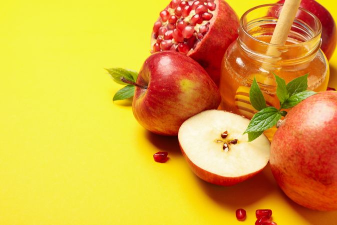 Honey pot with slices apples and pomegranate on yellow table with text for space
