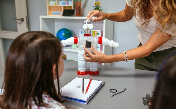Teacher in a robotics class explaining how connect solar panel on recycled toy robot