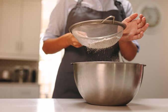 Close up shot of female chef sifting flour in bowl