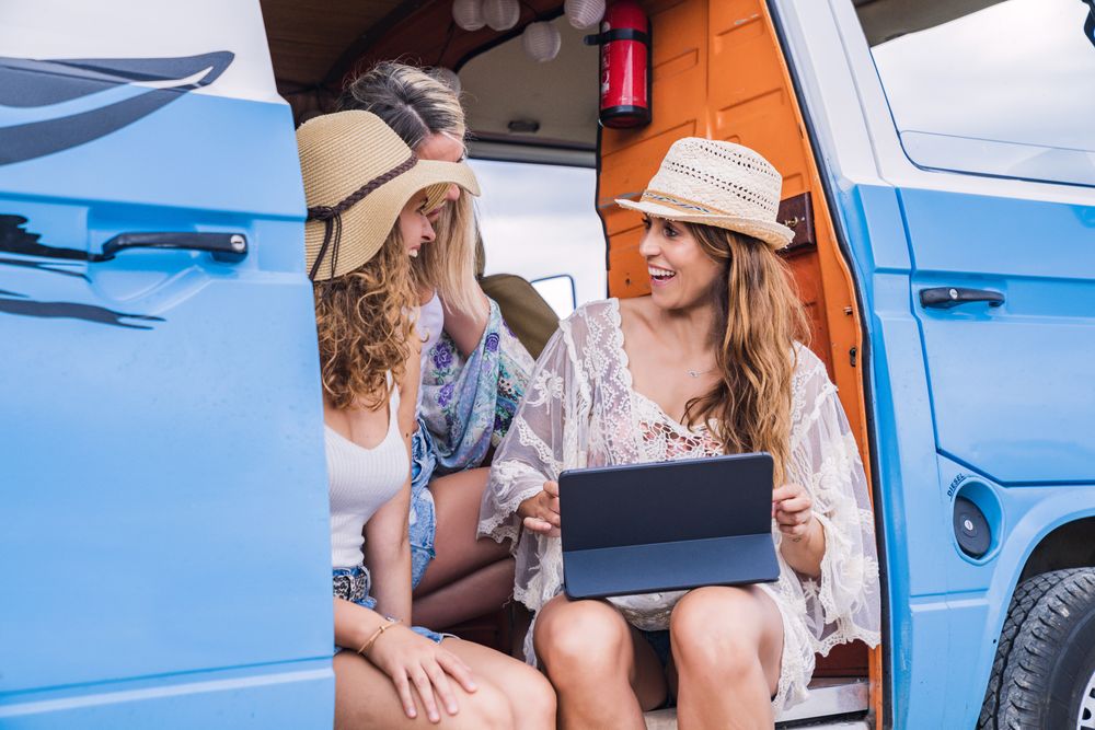 Lively women in hat speaking with tablet on knees sitting in open car