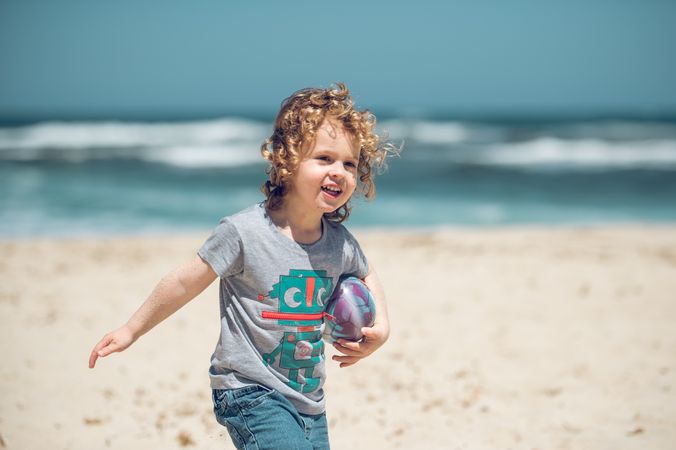 Cheerful boy with ball walking on beach