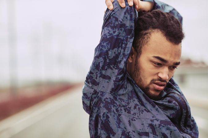 Fit male stretching arm before starting workout outdoors