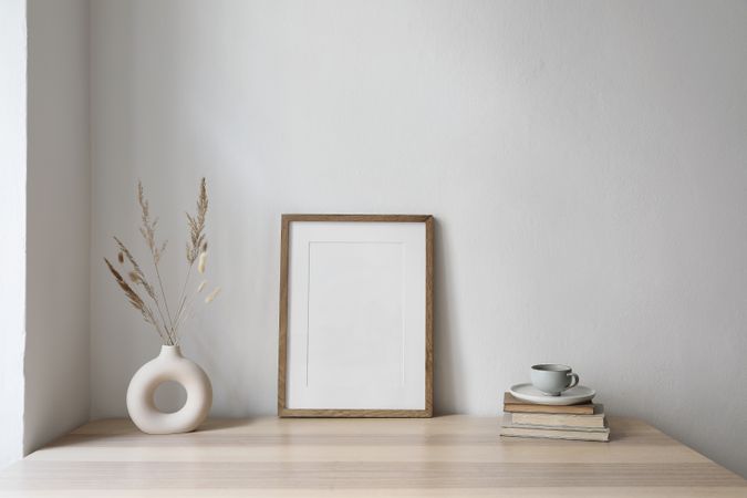 Elegant neutral poster mockup of wooden picture frame on beige table with modern boho vase with dry grass and old books
