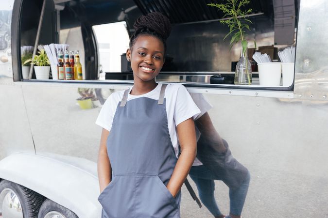 Happy Black woman in apron standing proudly outside her food truck