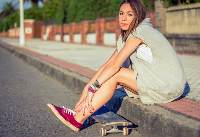 Young girl with skateboard sitting outdoors on summer