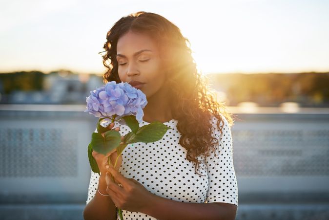 Black female smelling a blue flower backlit by sun