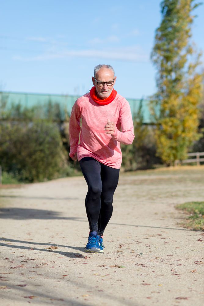 Grey haired man in red shirt and glasses exercising outside looking down