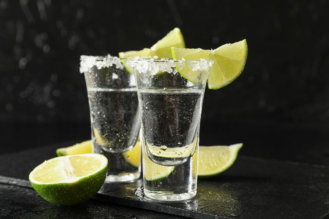 Tequila shots with salt and lime slices on dark background