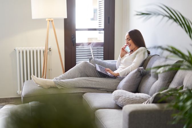 Smiling woman browsing on laptop and sitting on settee
