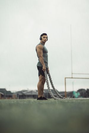 Athletic man holding battle ropes in the rain on football field