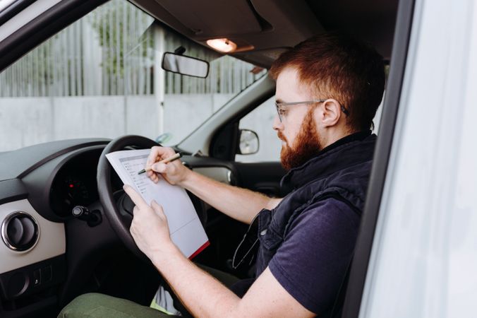 Courier filling papers while preparing for delivery of order to client in car