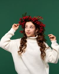 Girl adjusting red berry wreath, looking up curiously.