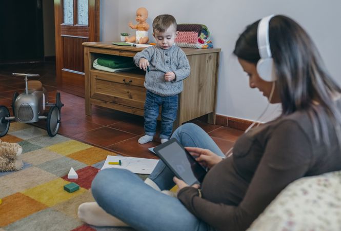 Pregnant using the tablet while her son is playing