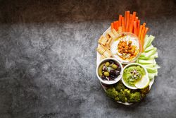 Tasty hummus and sauces decorated with bright cut vegetables on table
