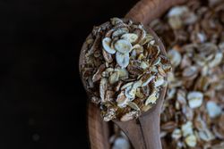 Close up of wooden spoon with oat grains over bowl