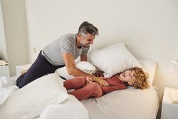 Laughing man tickling boy on bed