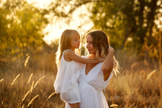 Woman carrying little girl in marsh at sunset