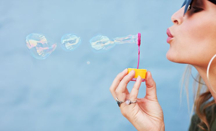Close up side view shot of young female model blowing soap bubbles on blue background