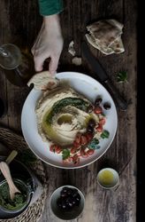 Crop hand dipping flatbread into hummus pesto with tomatoes and beans
