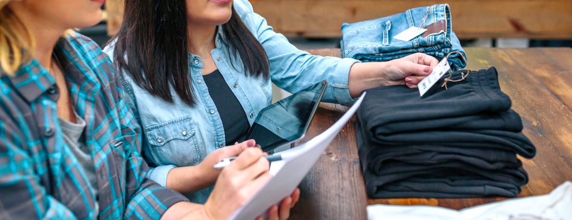 Banner of unrecognizable female entrepreneur checking label of pants on stack in clothing shop