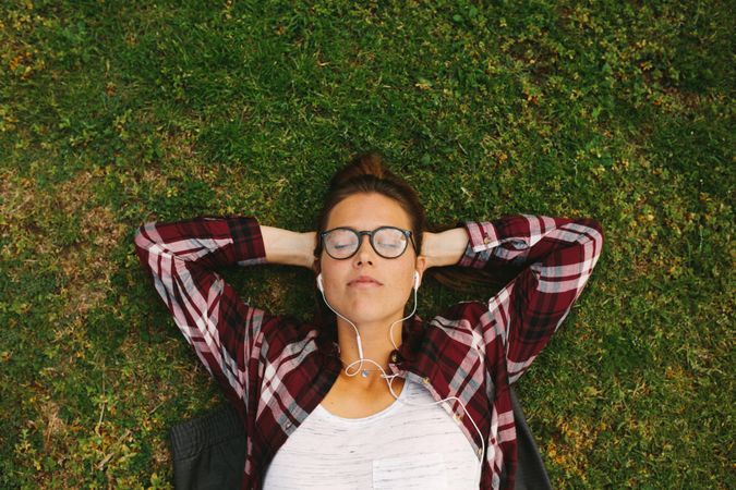 Top view of young woman wearing eyeglasses listening to music with earphones