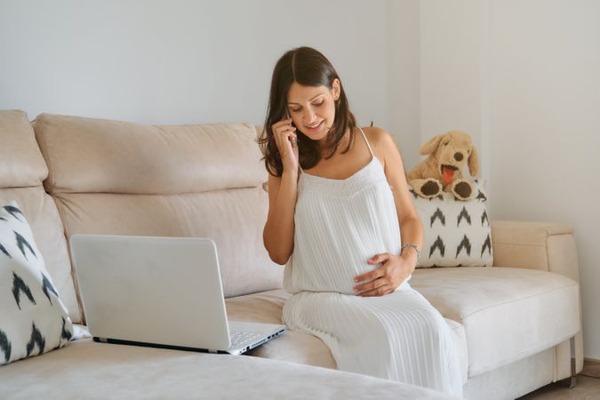 Happy expecting female touching tummy and talking on phone