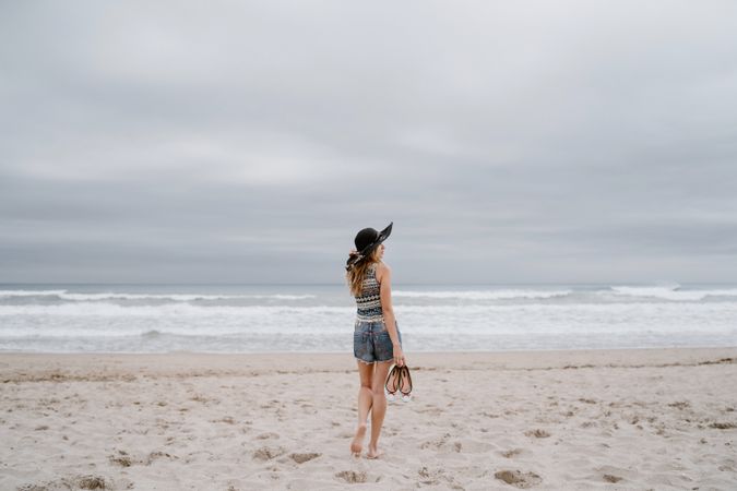 Young female walking barefoot on sandy beach