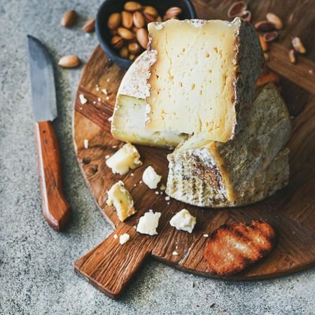 Wheel of cheese on wooden board, with knife and peanuts