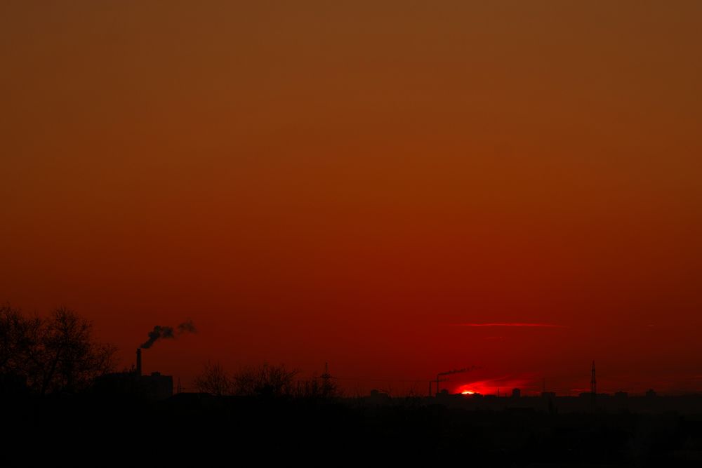 Fiery red sun dipping below horizon with industrial smoke