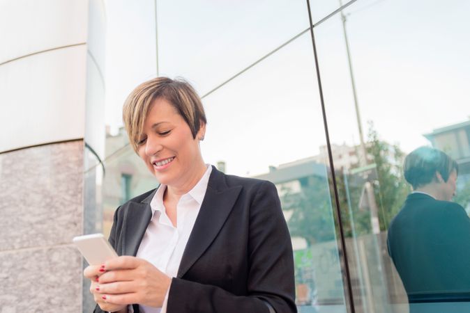 Businesswoman in blazer texting on cellphone outside building