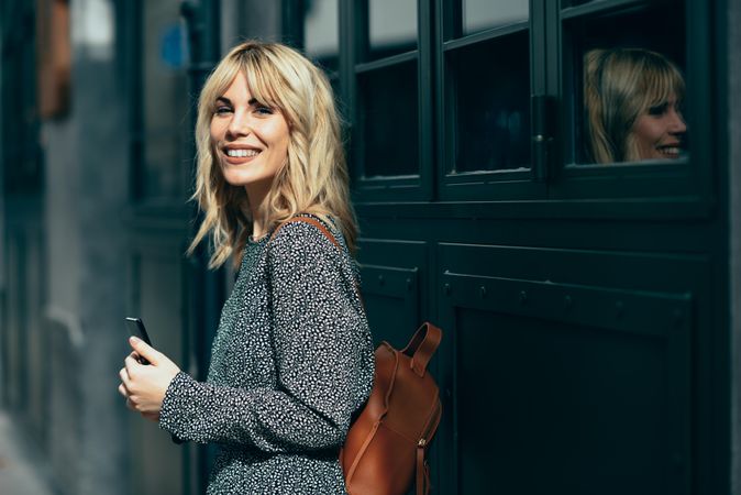 Smiling blonde female wearing casual clothes outdoors with cell phone, copy space