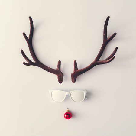 Brown antlers making reindeer face with sunglasses and bauble on light background