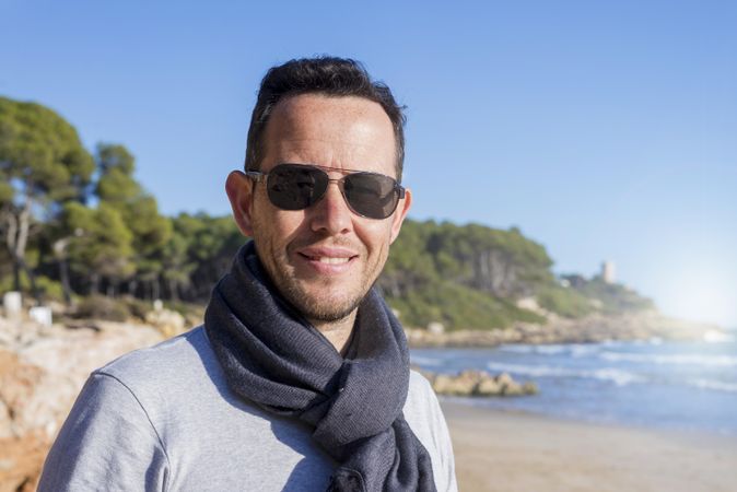 Male standing on coast on bright day and smiling