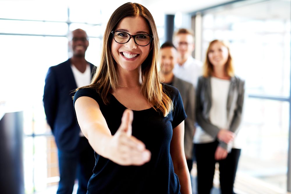 Businesswoman pictured in a bright office in front of her colleagues with outstretched hand