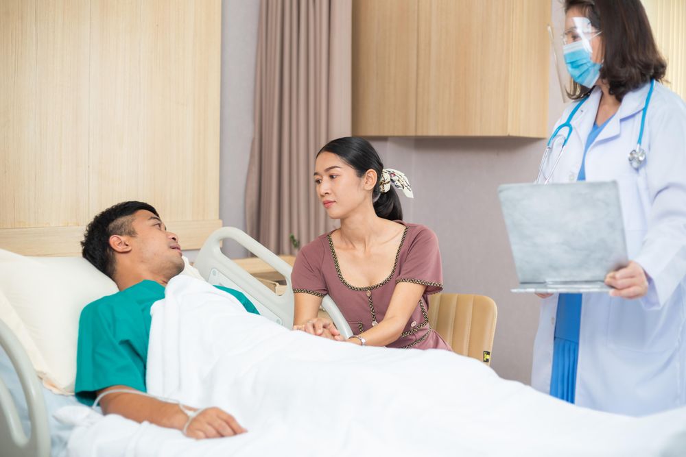 Couple in hospital having doctor treating male in bed
