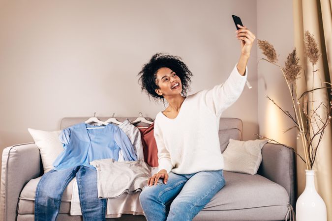 Woman taking selfie surrounded by clothes on a couch
