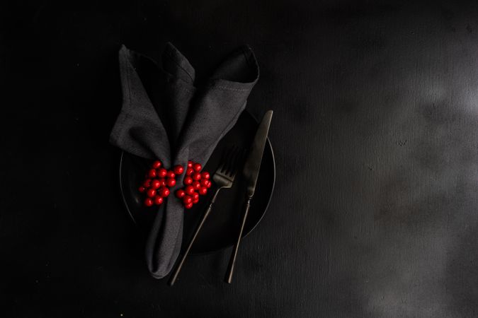 Holiday table setting with dark cutlery, plate and table with red berries