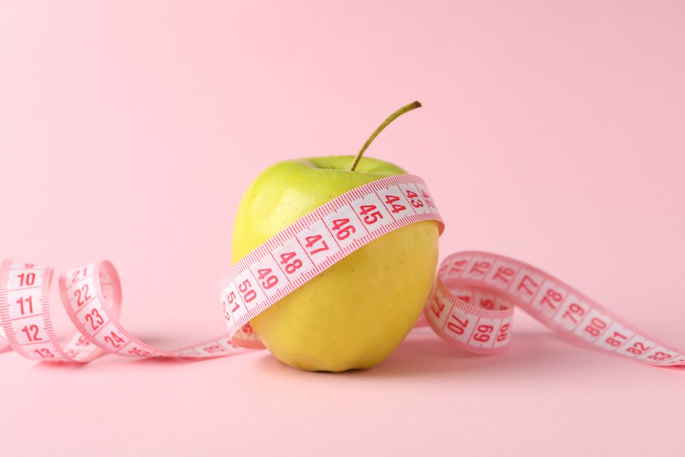 Measuring tape with apple on pink background, weight loss